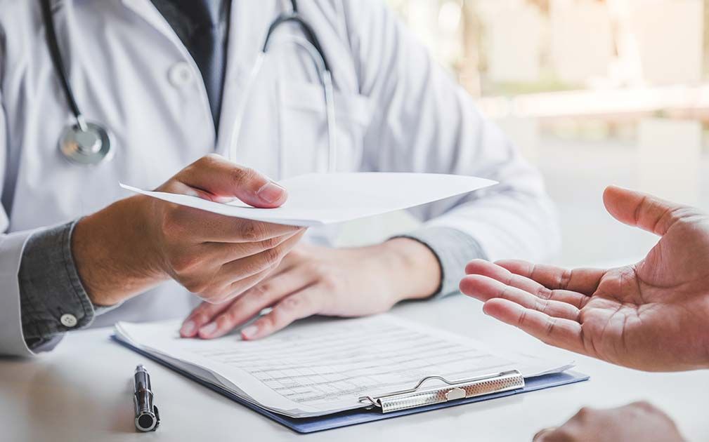 Doctor handing a prescription to a patient; hands, white coats, paperwork.