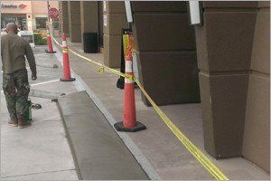 Man walks past freshly poured concrete. Yellow caution tape and traffic cones block access in front of a building.