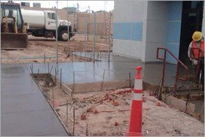 Construction site: fresh concrete, rebar, worker with hard hat, water truck, orange cone.
