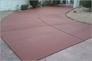 Red concrete driveway with curved design, plants on the side, and a sunny setting.