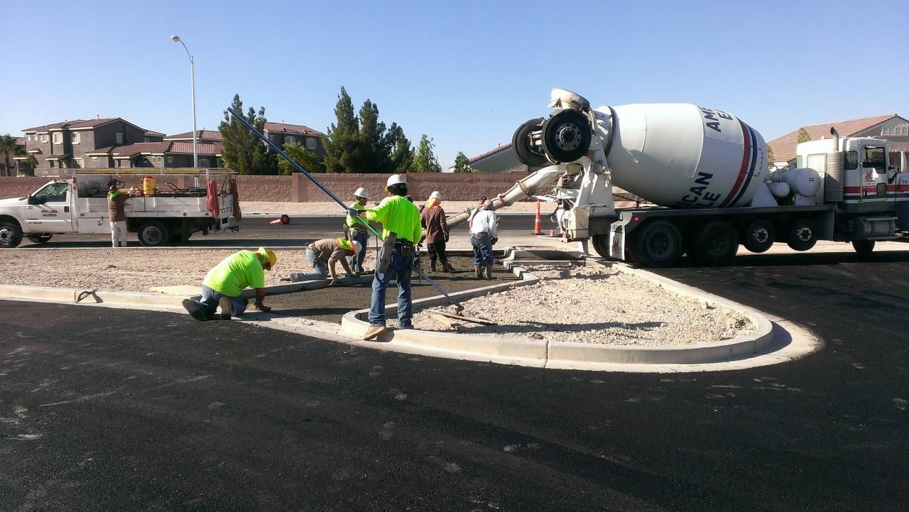 Construction workers pouring concrete from a truck into a roundabout on a sunny day.