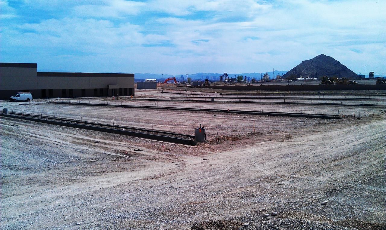 Construction site with a building, dirt, and a mountain in the background under a cloudy sky.