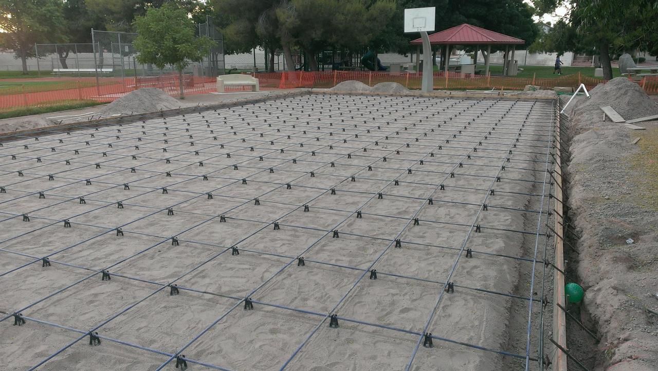 Construction site with grid of pipes and black supports, possibly for a sports court. Green pipe at the edge.