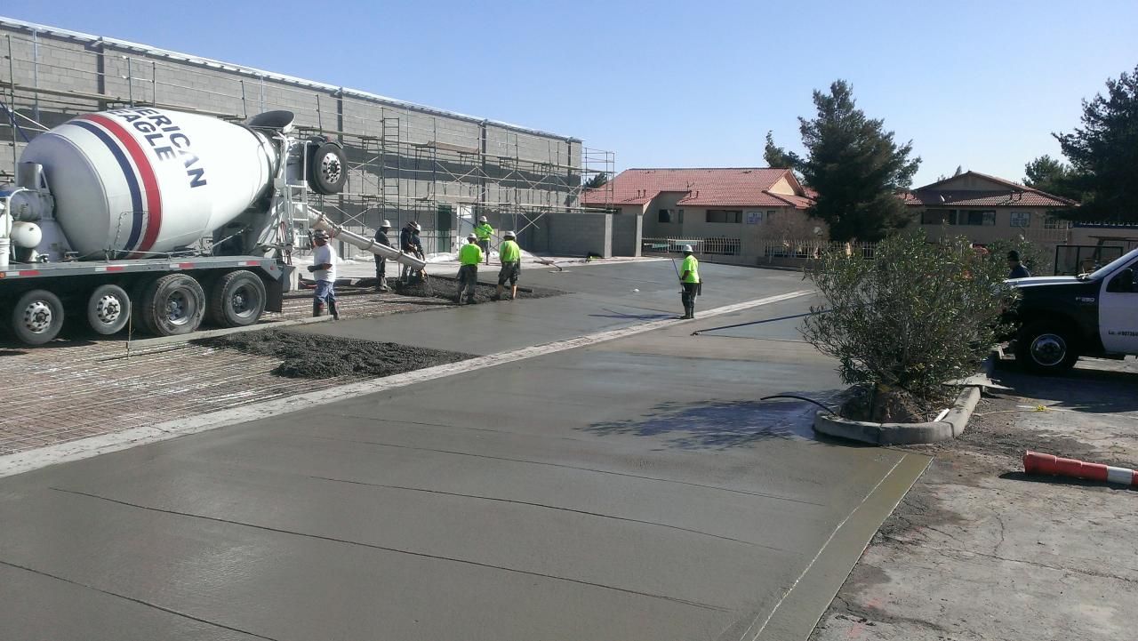 Concrete being poured from a truck onto a new driveway by construction workers wearing safety vests.