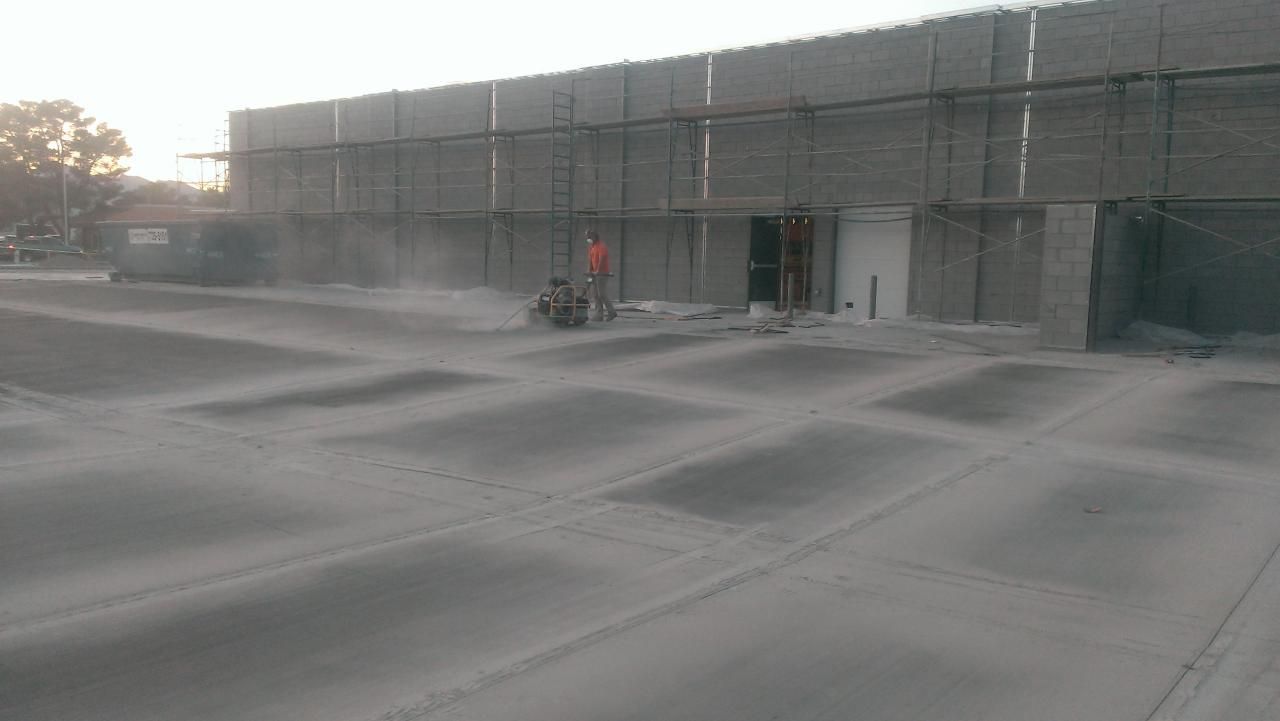 Construction site; worker using saw. Exterior of building with scaffolding. Concrete ground with marked squares.