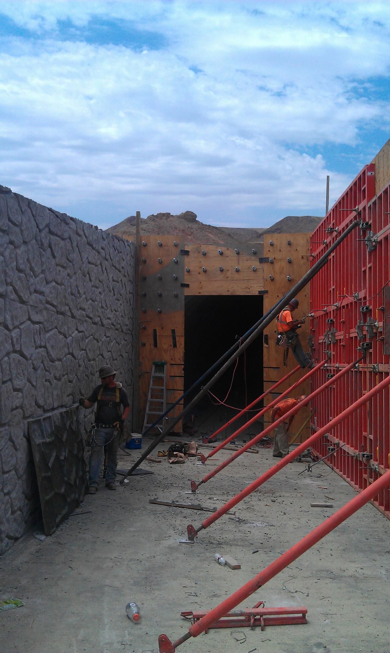 Workers near a rock wall and red formwork