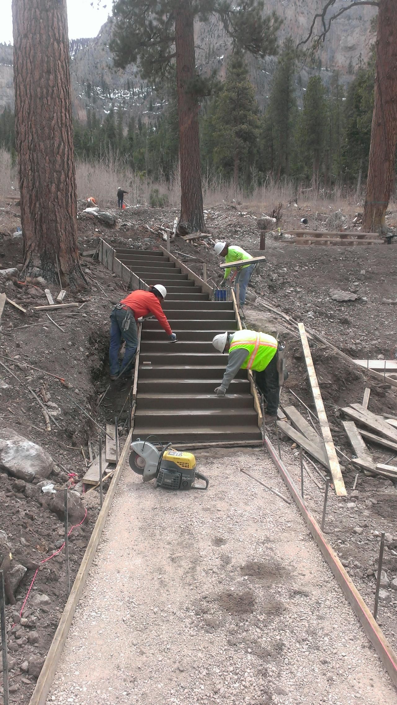 Construction workers building concrete steps on a pathway in a wooded area.