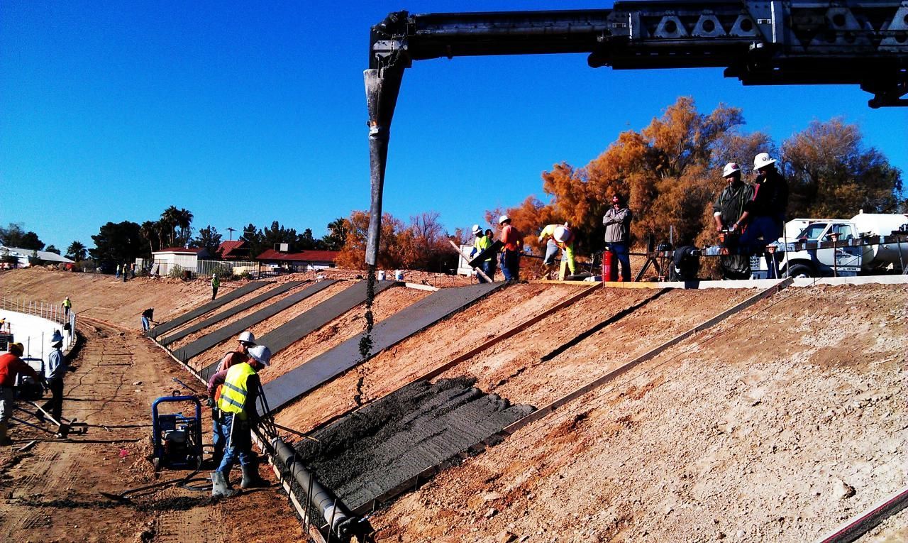 Construction workers pouring concrete on a hillside with a pump truck under a clear blue sky.