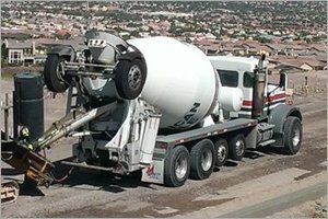 Concrete mixer truck tilted back, discharging concrete. White drum, setting is a residential area.