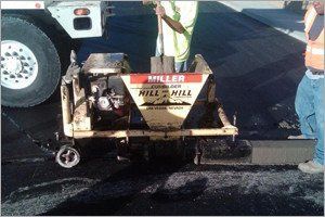 Road crew using a Miller curb machine. Dark asphalt, workers in safety vests.