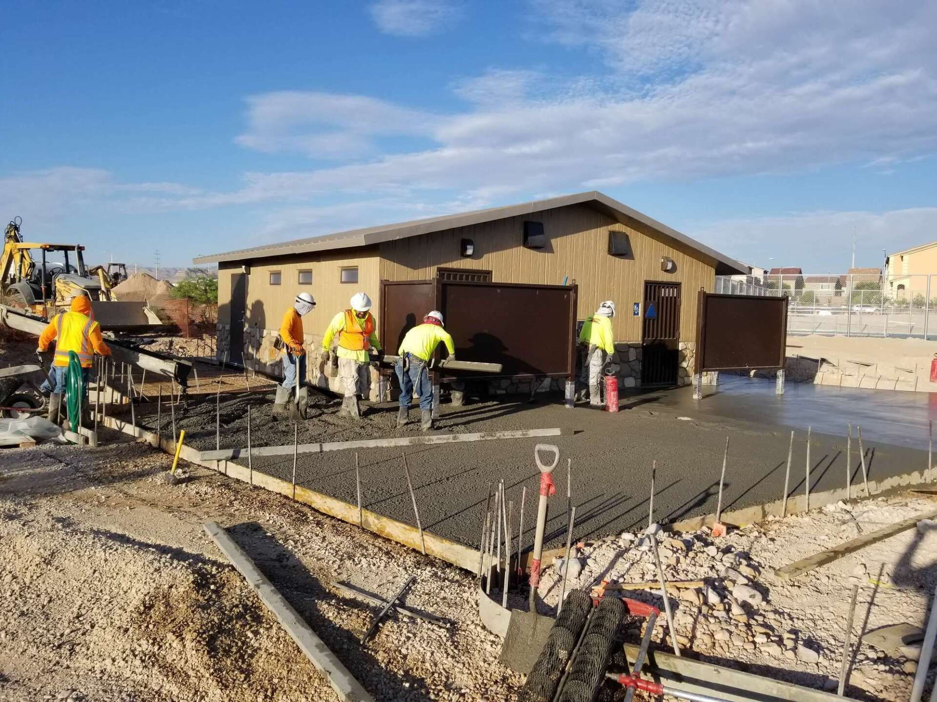 Construction workers pouring concrete for a foundation, building in the background, clear sky.