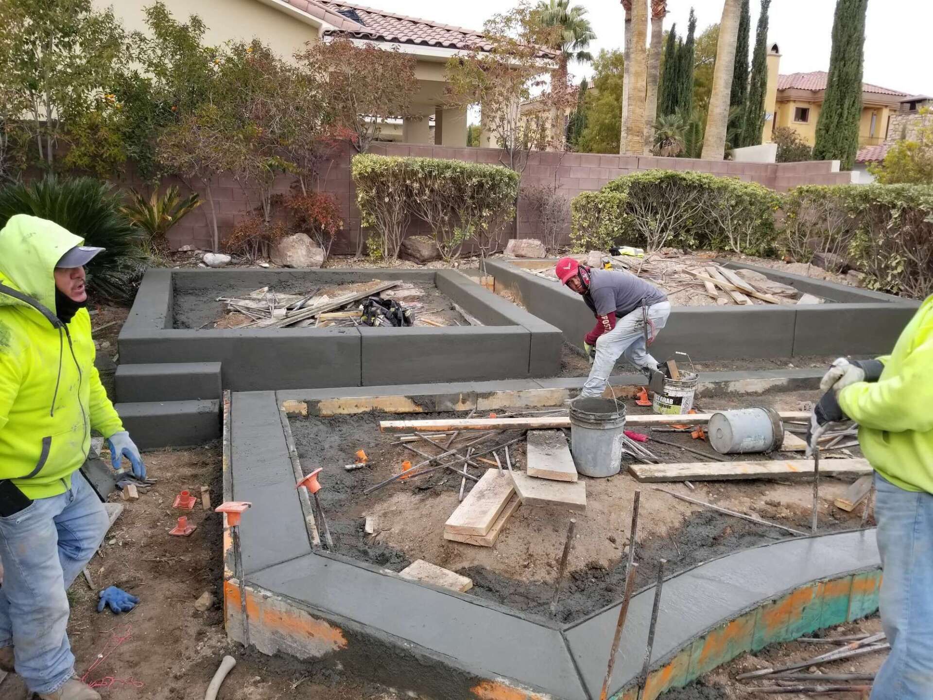 Construction workers pouring concrete for raised garden beds outdoors.