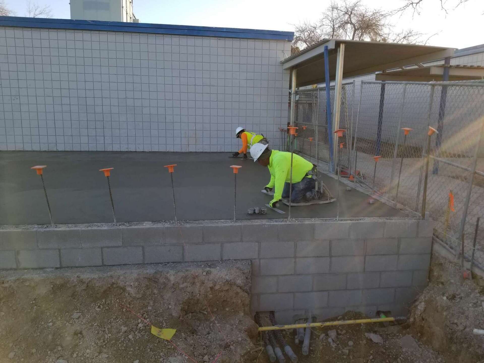 Construction workers pouring concrete on a block foundation, outdoor setting.