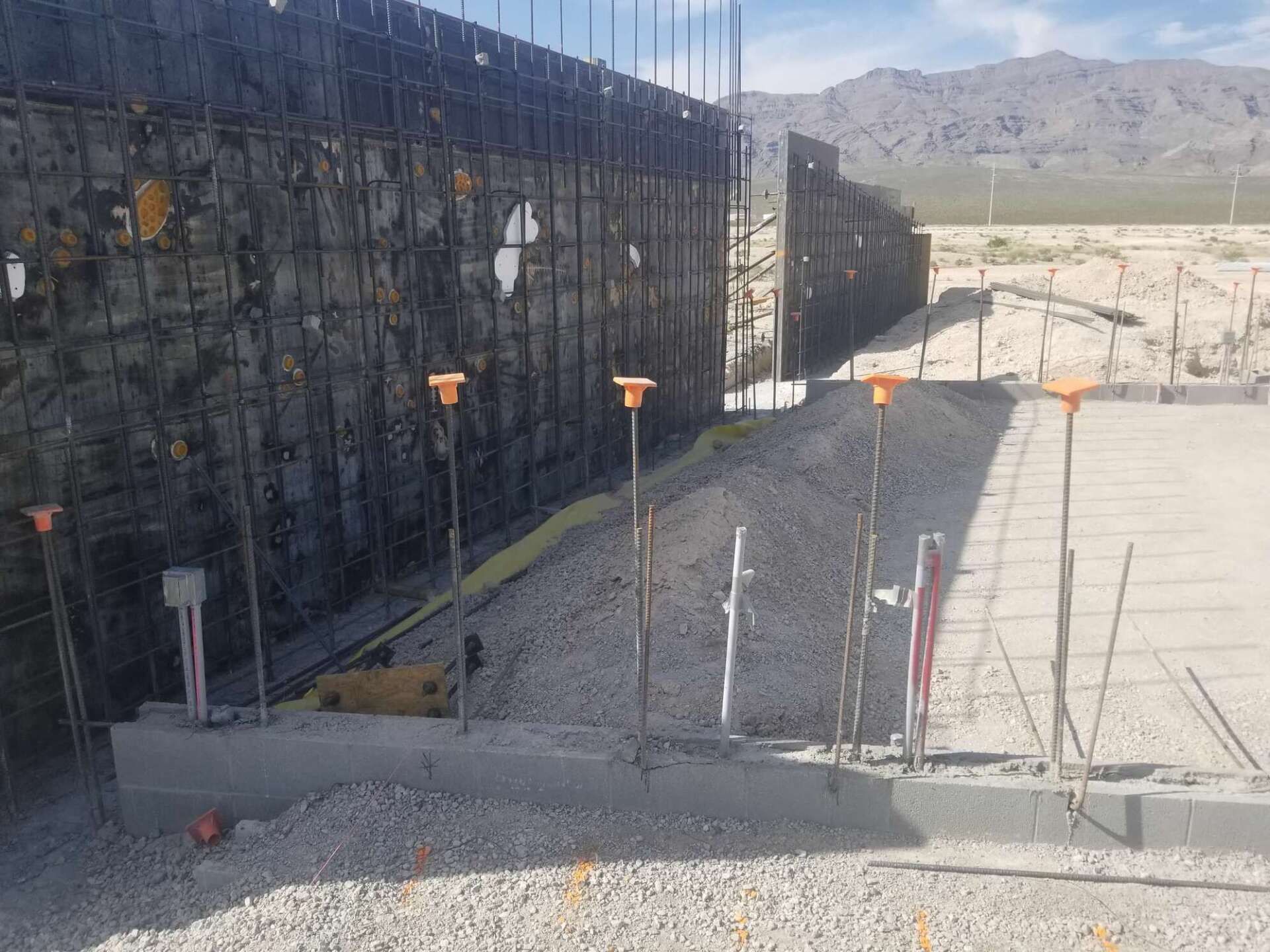 Construction site: Concrete base with rebar, gravel, and retaining wall.