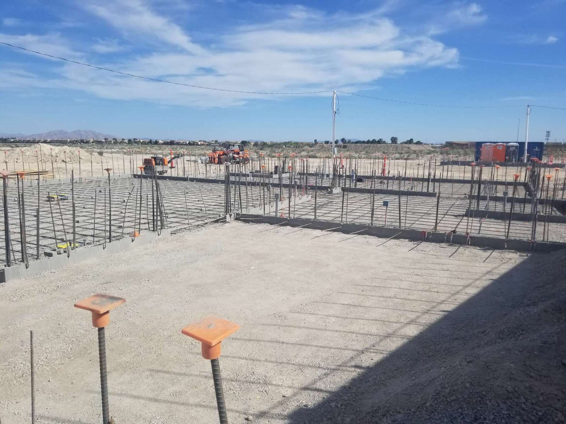Construction site with rebar framework and stakes against a blue sky.
