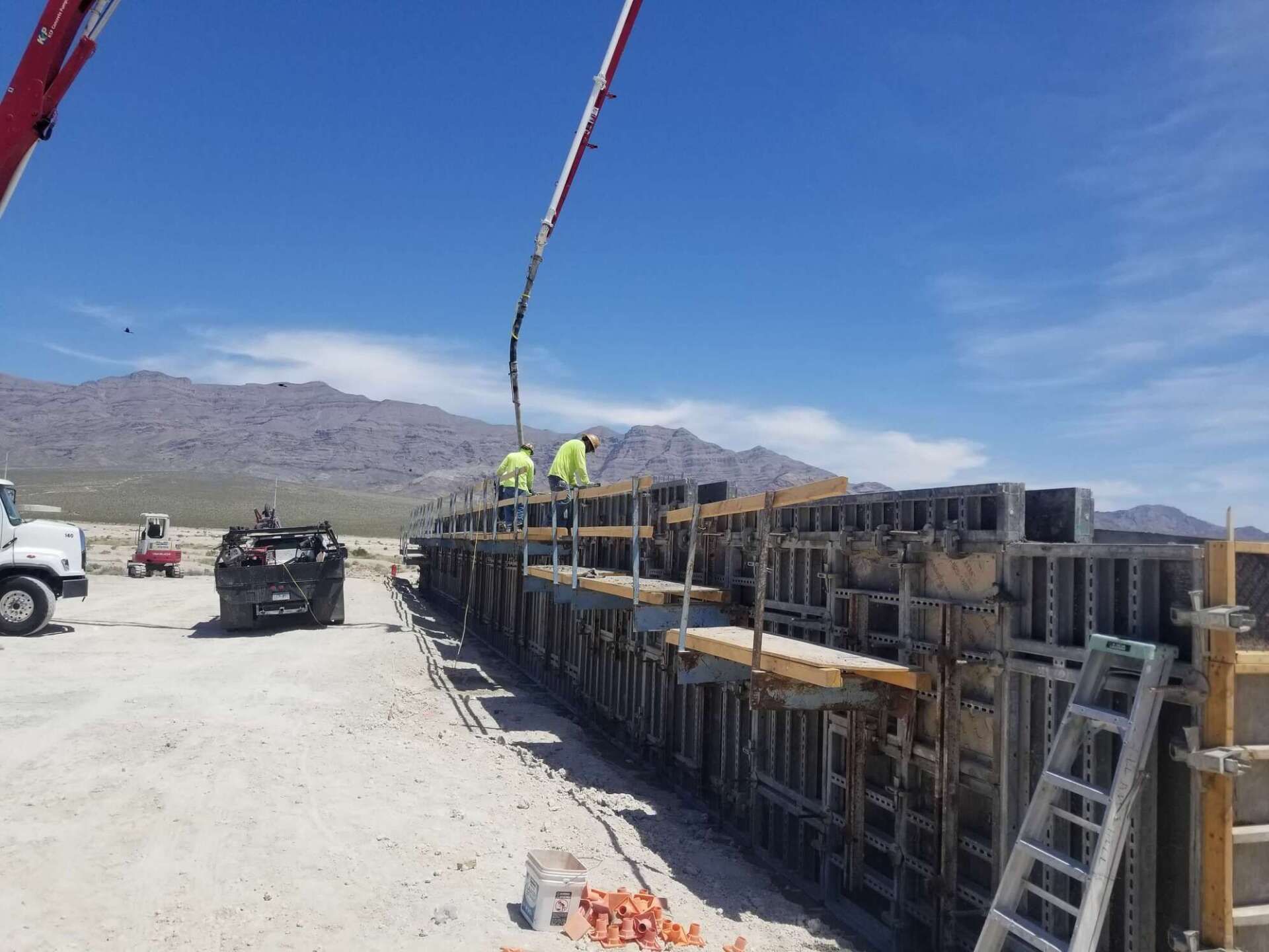 Construction workers pouring concrete into wall forms with a boom pump under a blue sky.