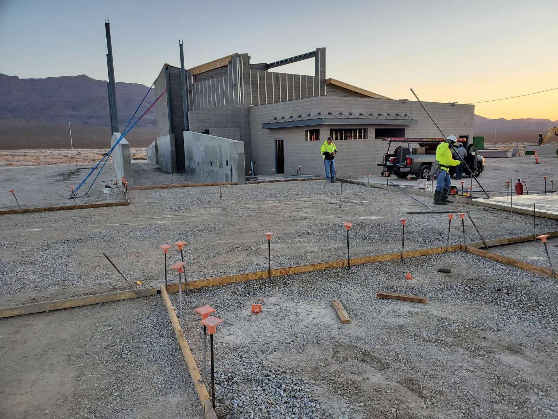 Construction site with building frame, workers, gravel, and forms for concrete.