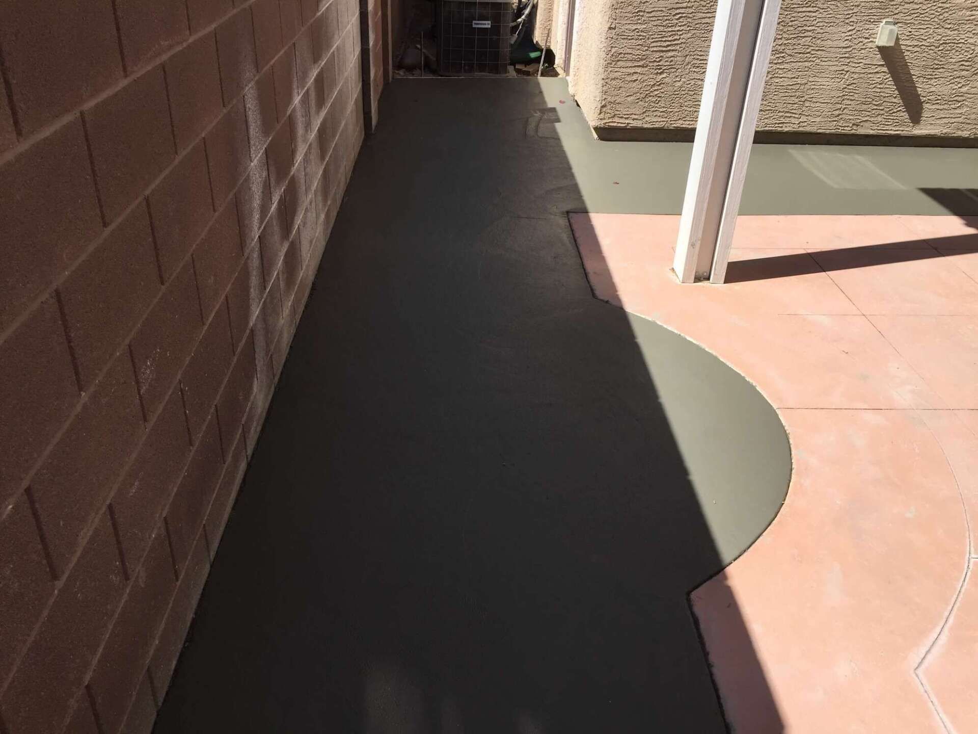 Dark gray painted concrete pathway between brick wall and patio with white support beam.