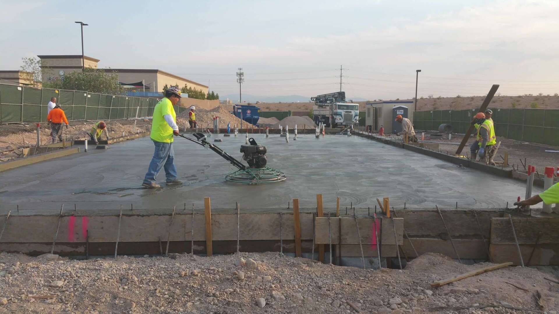Construction workers smoothing concrete slab with power trowel. Outdoors, daylight.