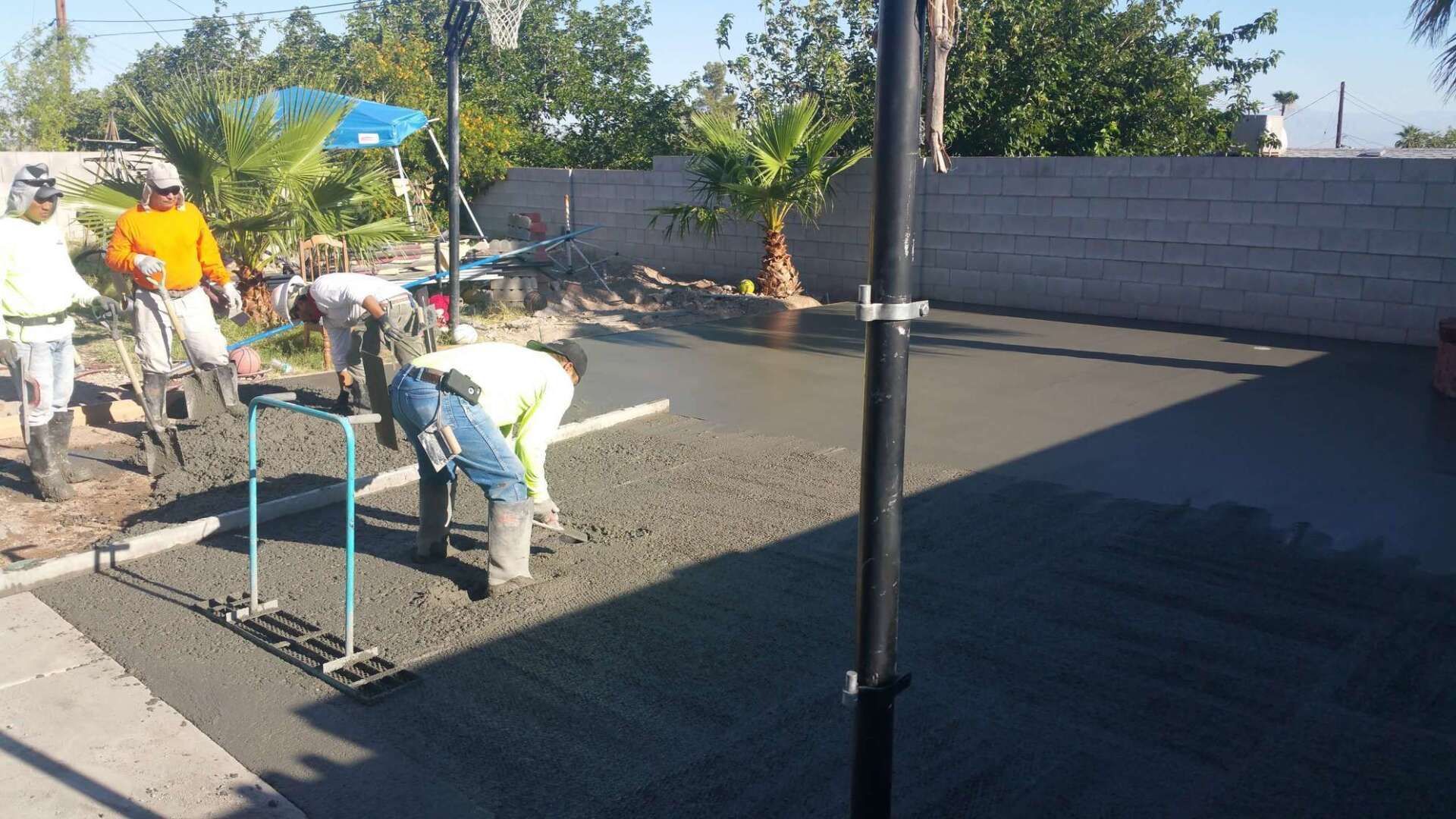 Workers leveling wet concrete in a backyard, using tools.