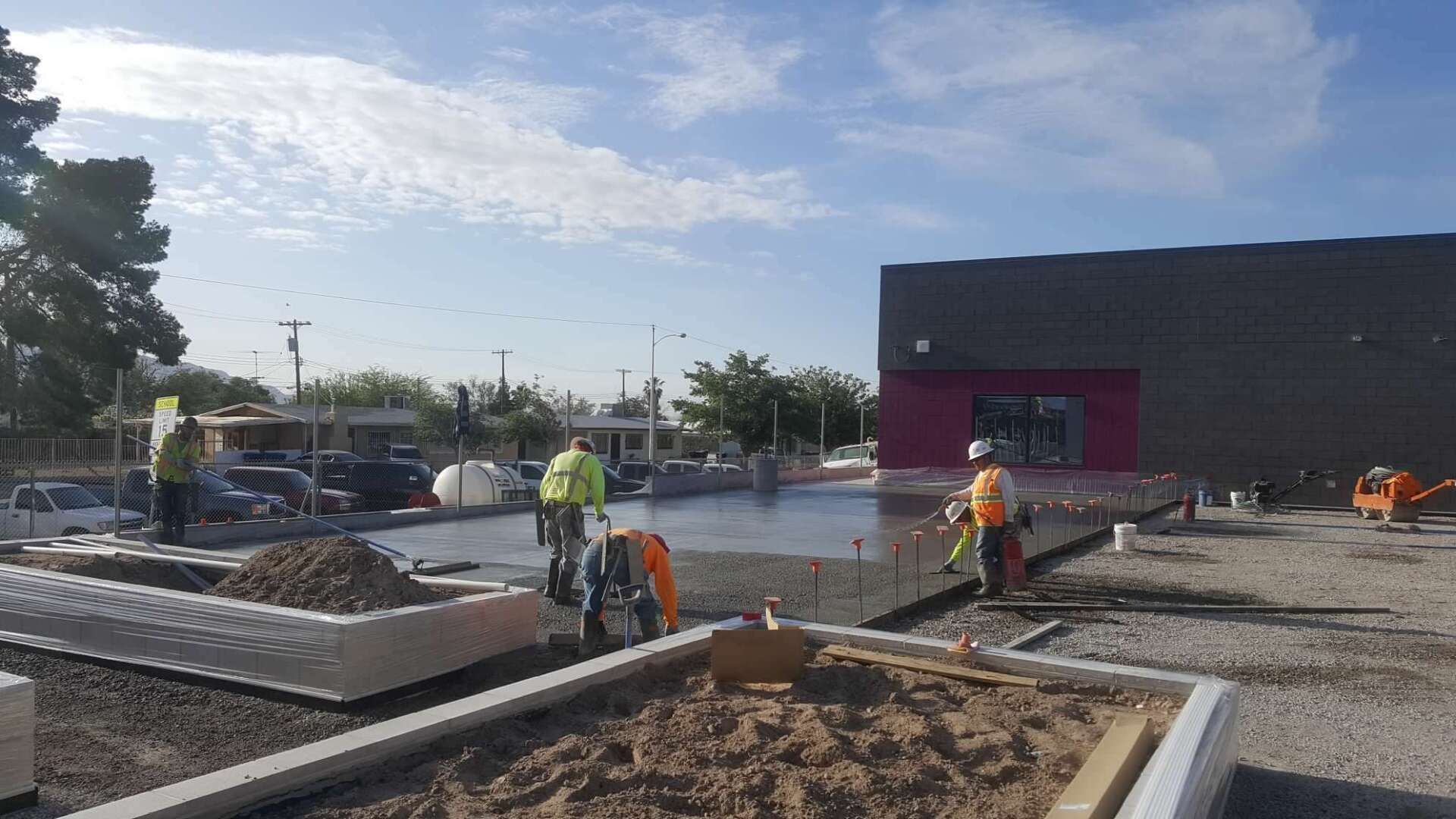 Construction workers smoothing concrete at a building site under a cloudy sky.