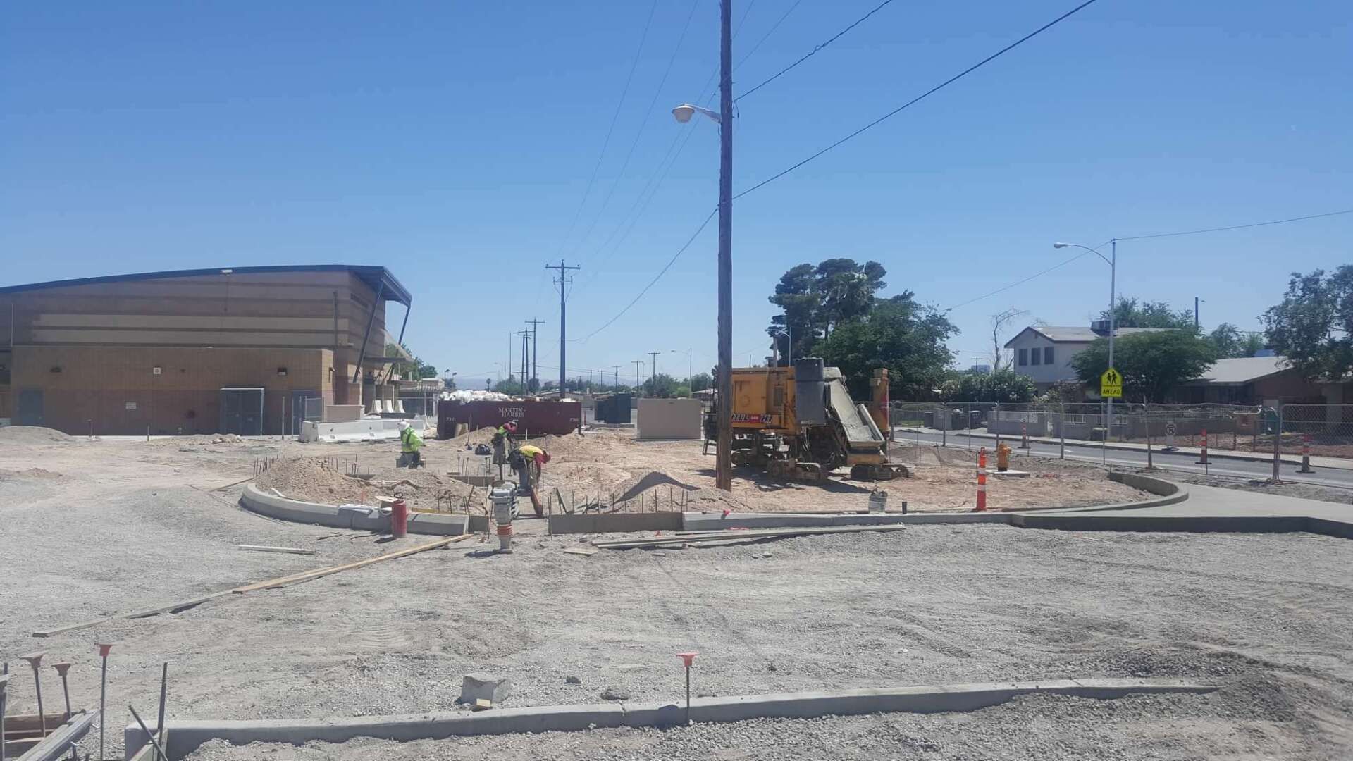 Construction site with workers, machinery, and concrete work underway on a sunny day.
