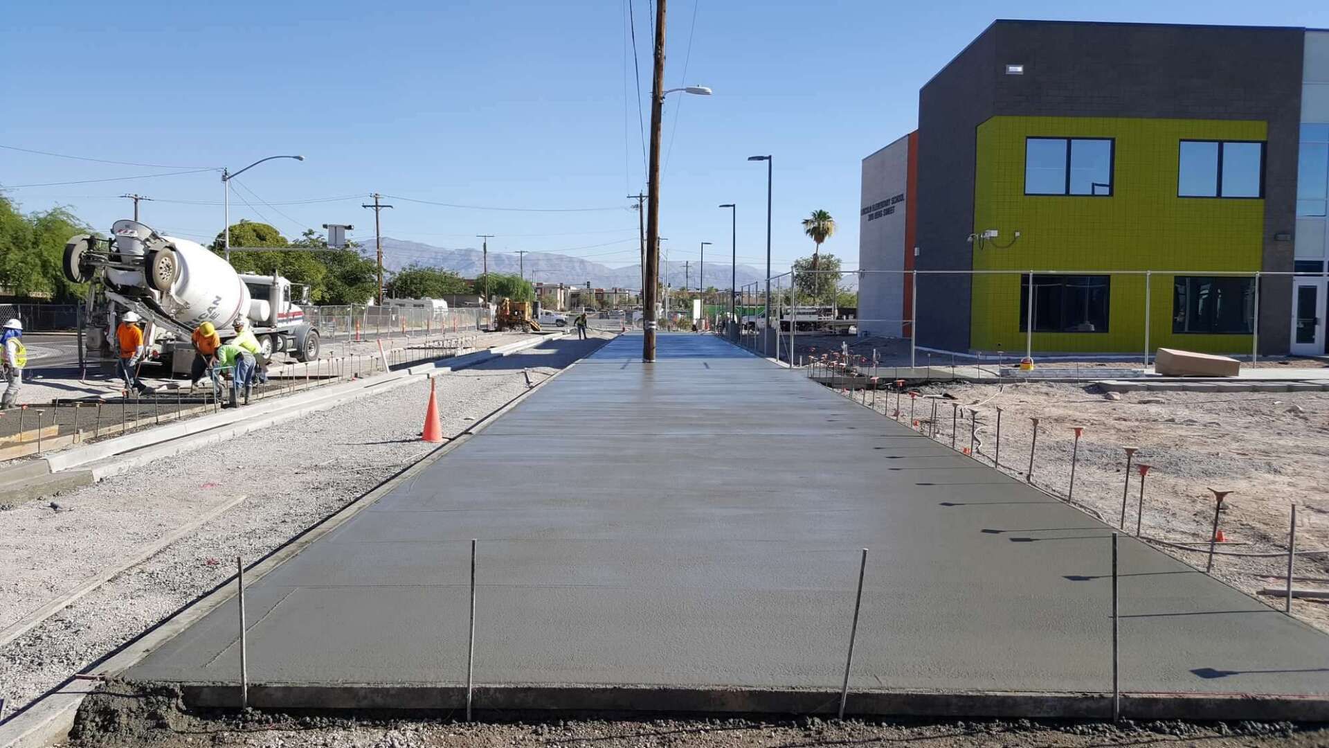 Freshly poured concrete sidewalk with a cement truck in the background, next to a building.