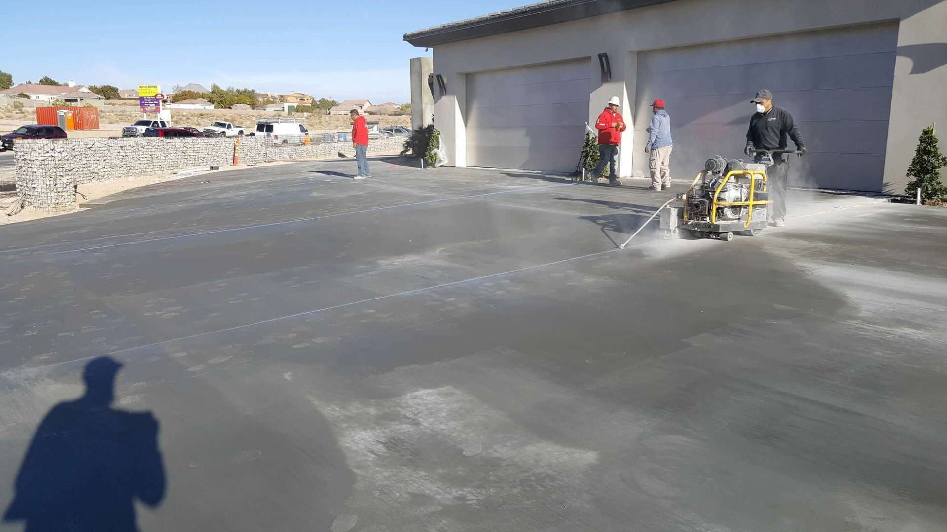 Construction workers cutting lines in wet concrete driveway in front of a house.