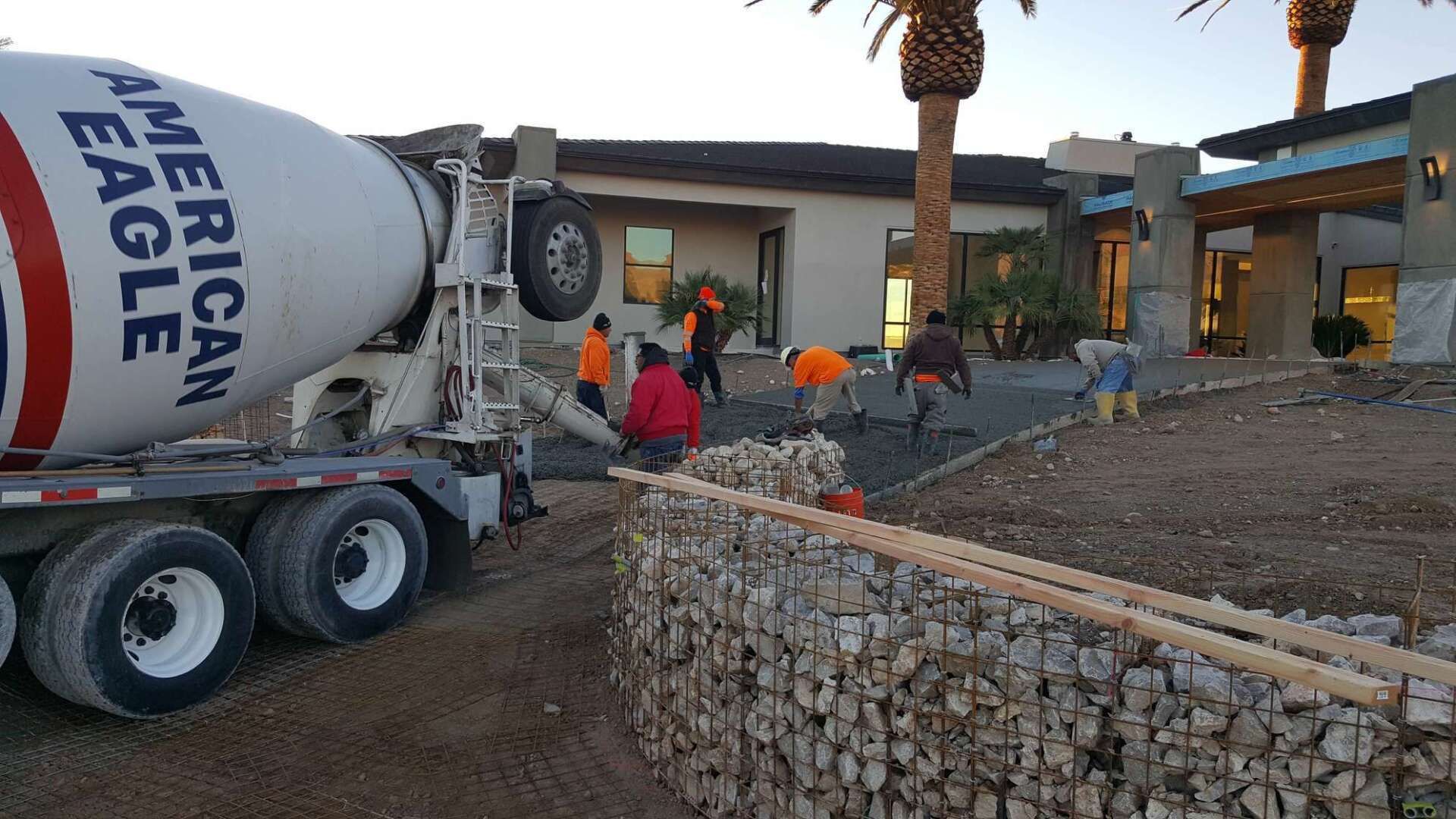 Concrete truck pouring concrete near a house, construction workers present, daytime.