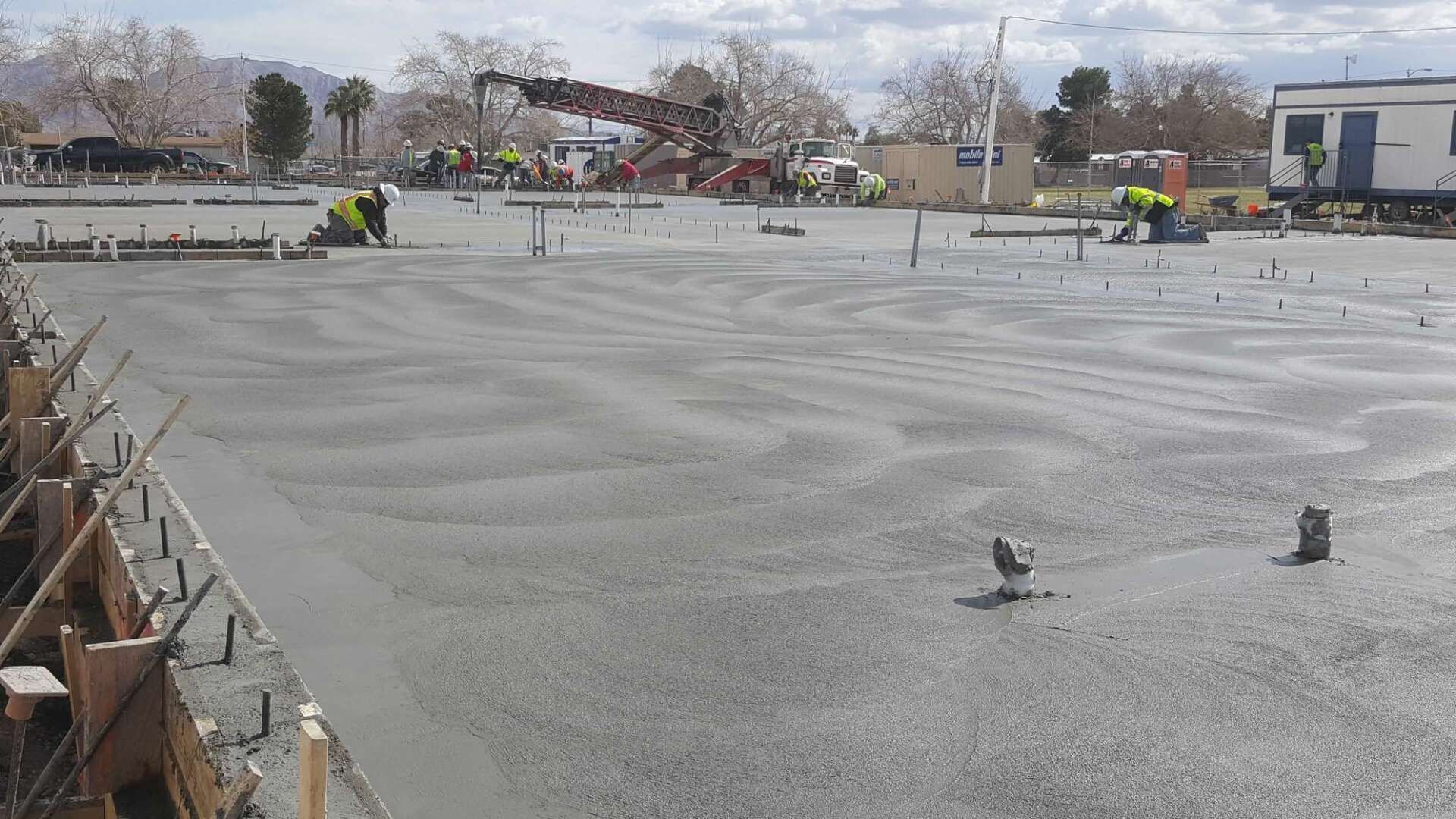 Freshly poured concrete slab at a construction site, workers in background, cloudy sky.
