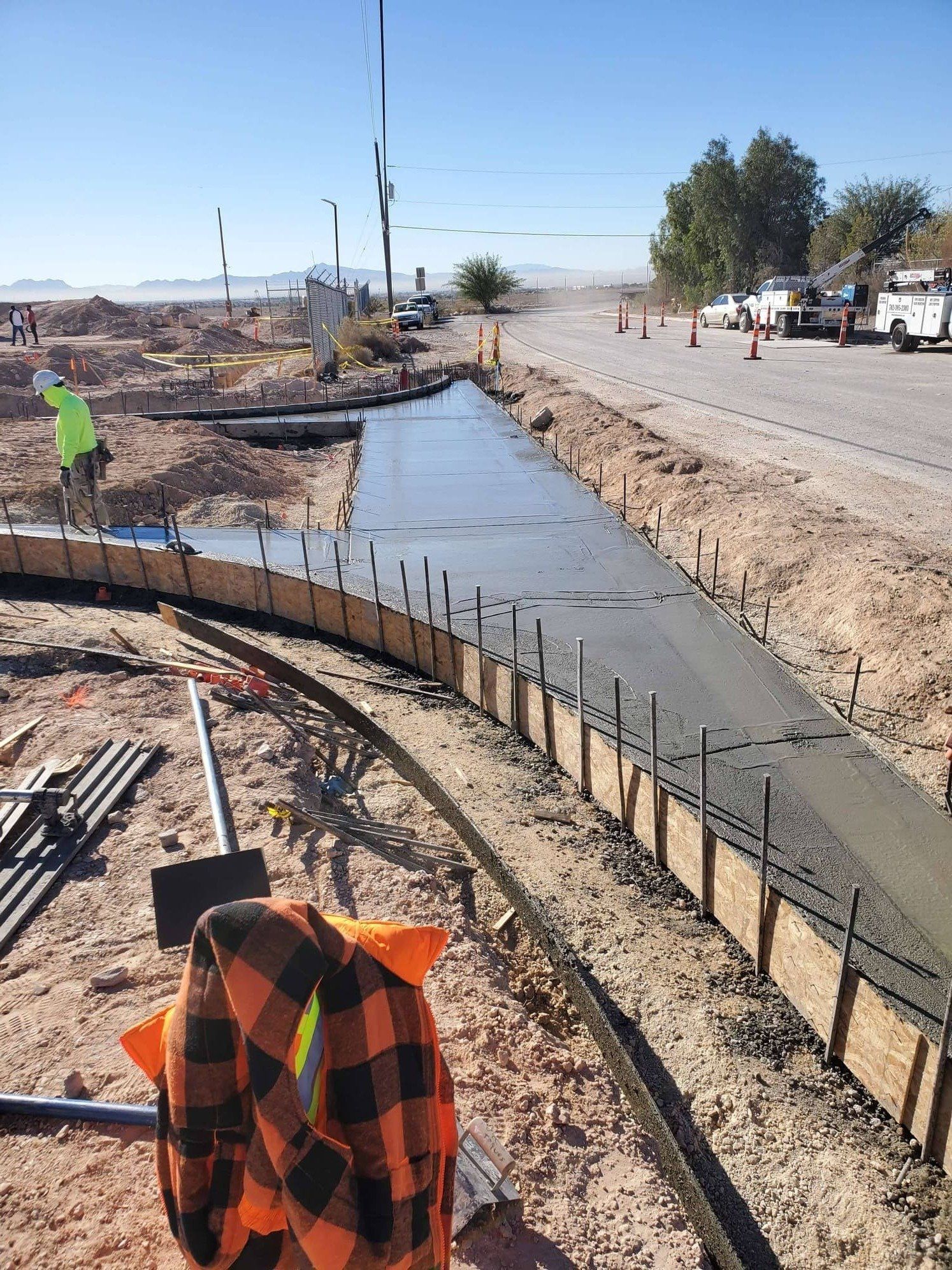 Construction site; worker pouring wet concrete into forms to create a curved sidewalk next to a road.