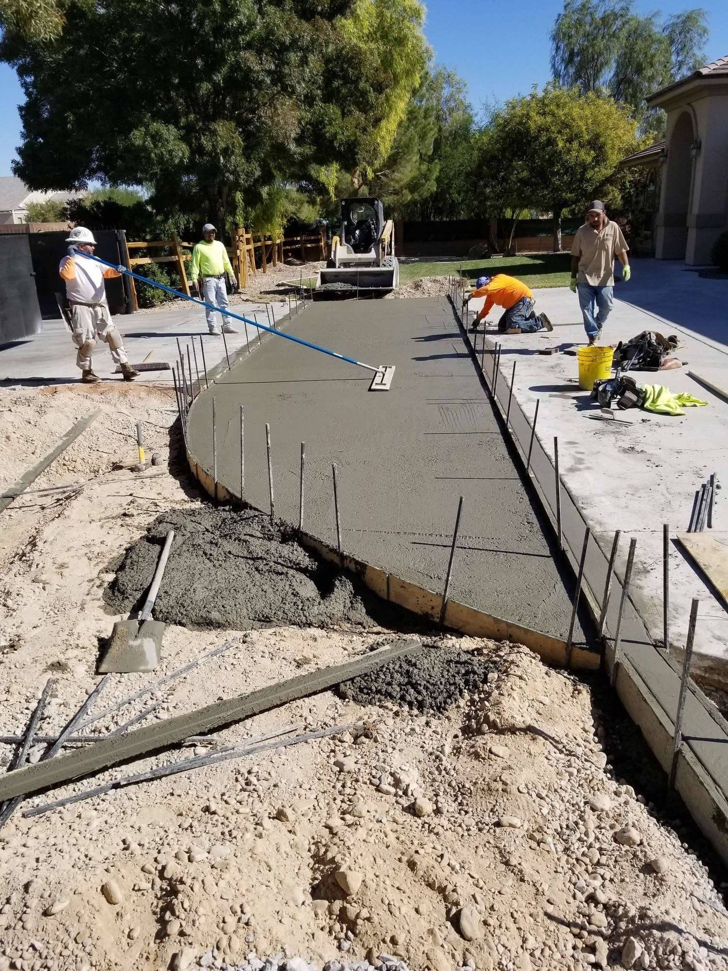 Construction workers pouring and leveling wet concrete for a driveway.