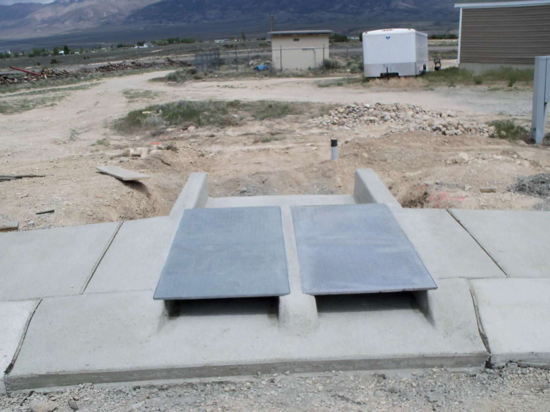 Concrete drainage channel with two metal grates, outdoor setting.