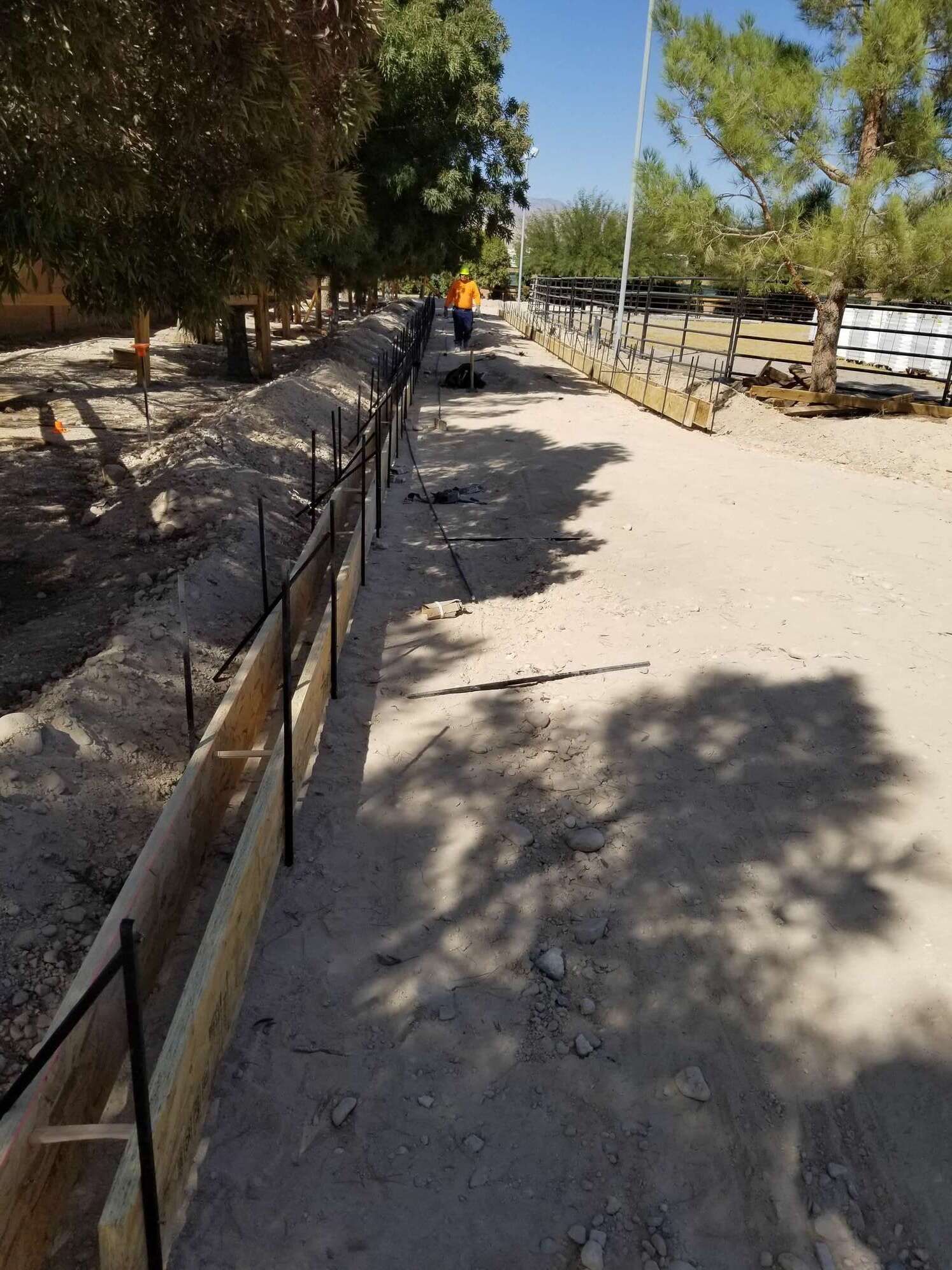 Construction site with wooden forms and rebar for concrete work; person in orange vest in background.