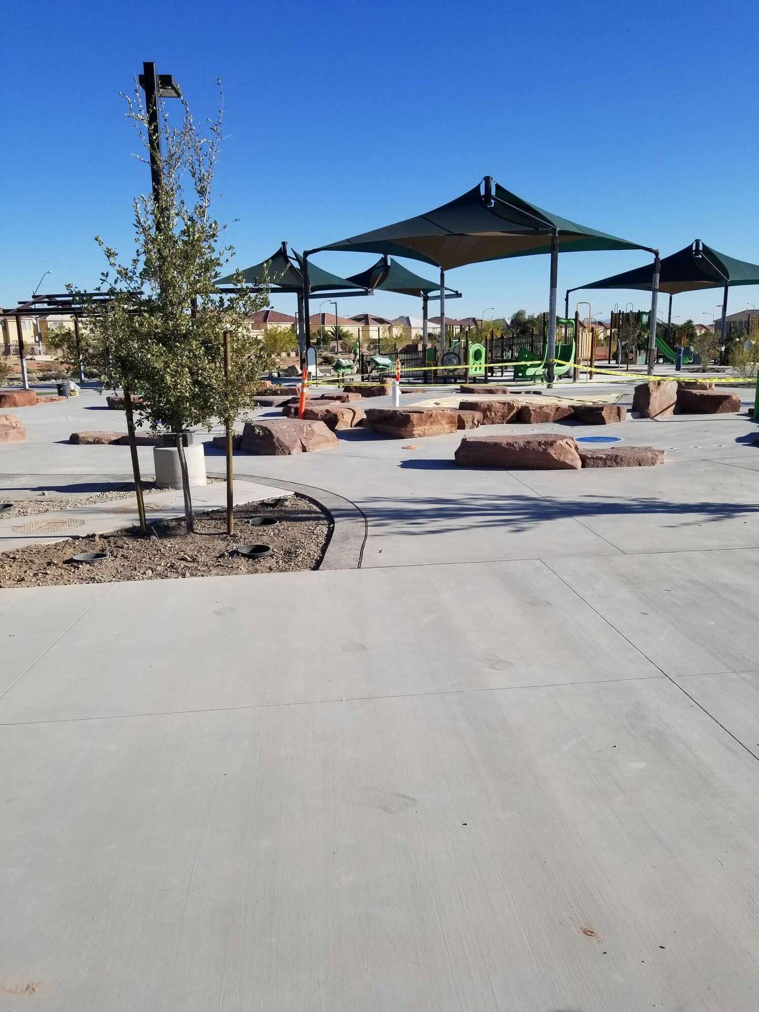 A concrete park area with shade structures and large stone platforms. Clear blue sky.