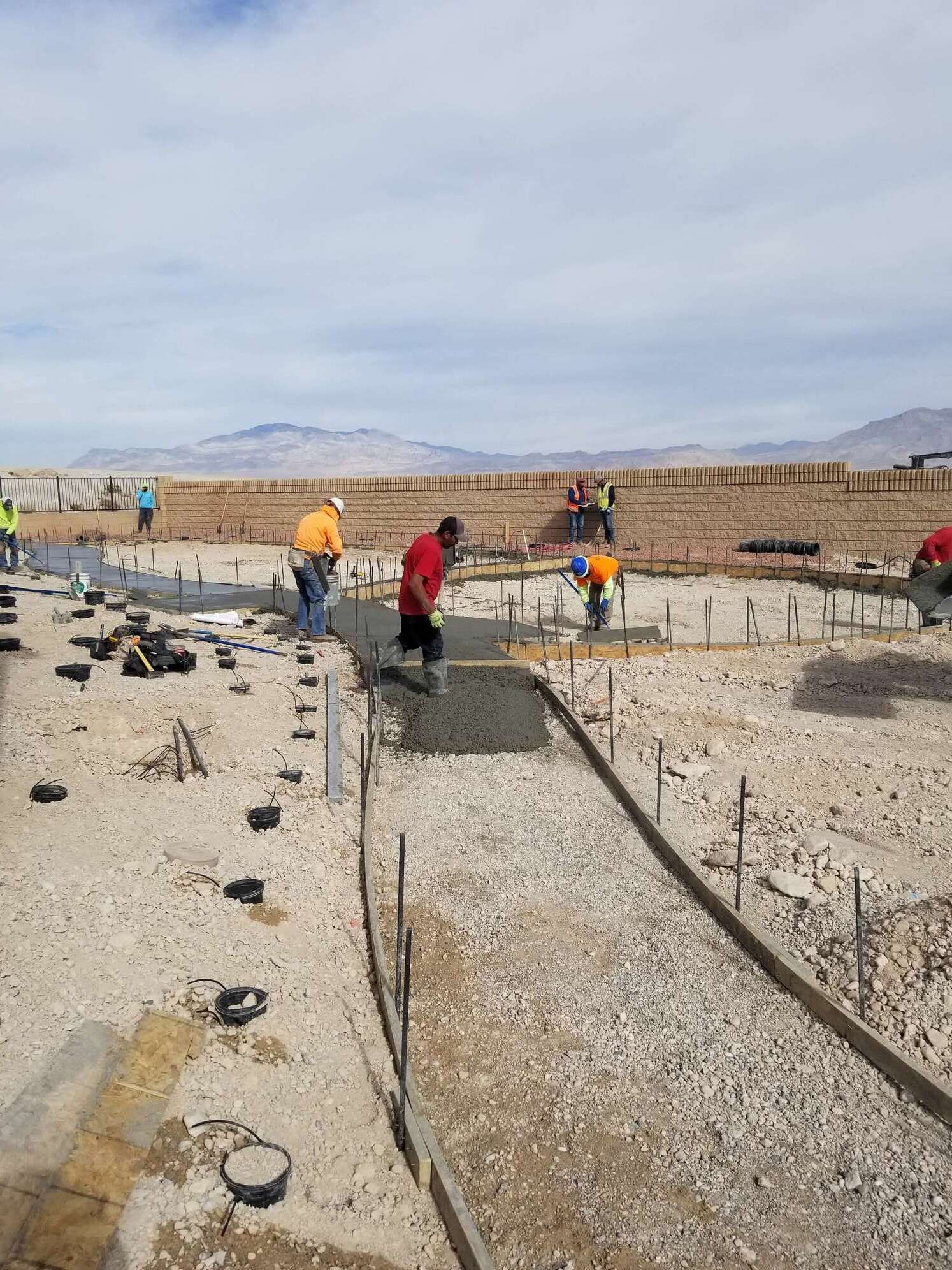 Construction workers pouring concrete on a gravel base outdoors on a sunny day.