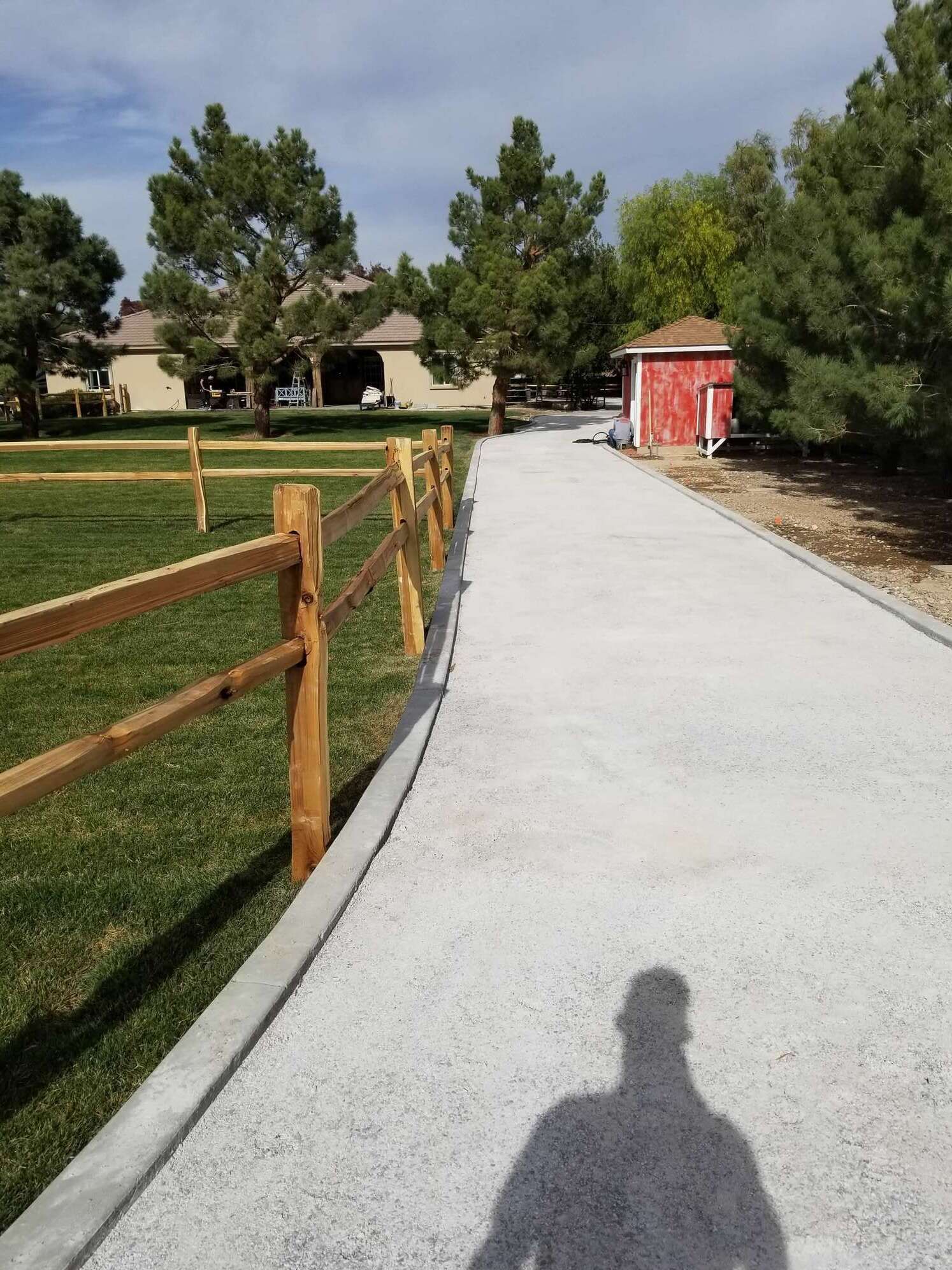 A gravel path curves through a park, with a wooden fence and trees on either side. A red shed sits on the right.