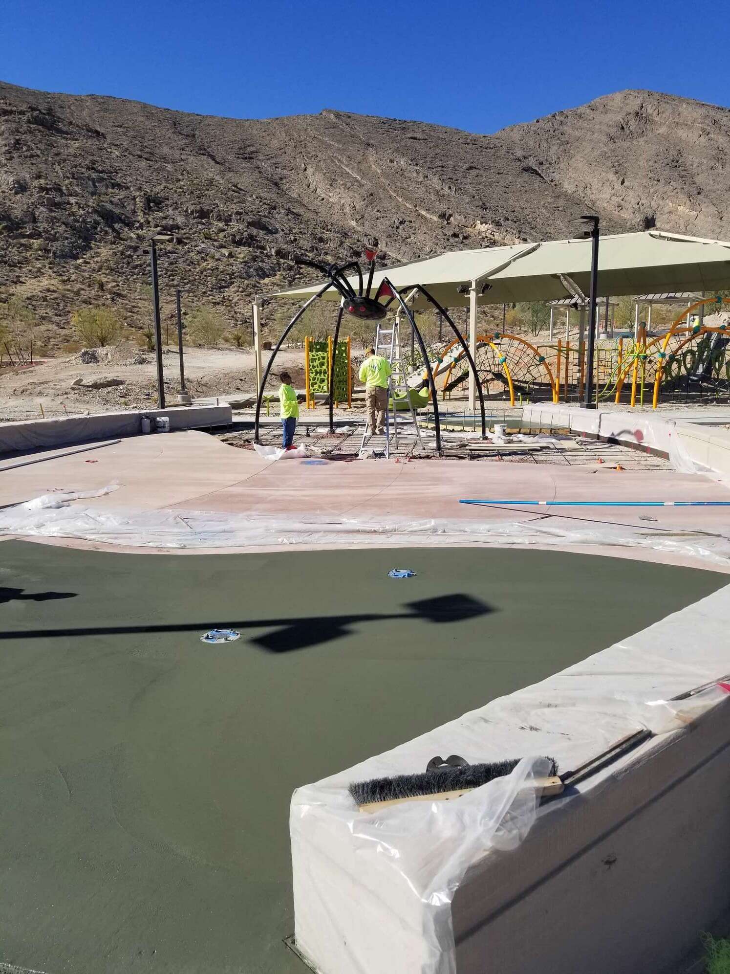 Construction workers installing water features in a desert playground, mountains in background.