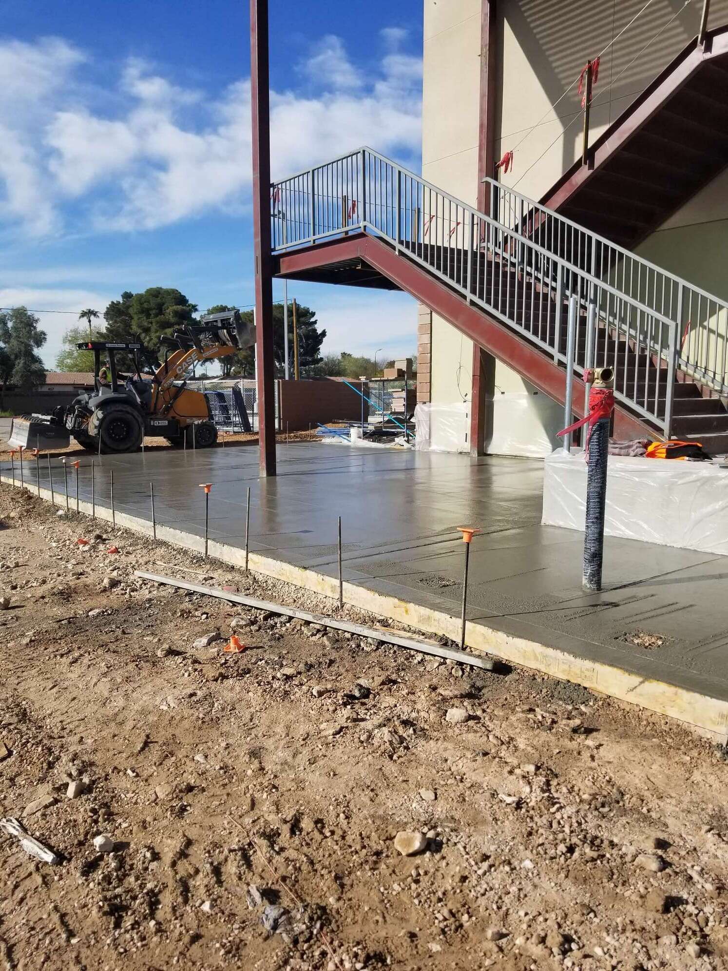Concrete being poured for a new building. Staircase and construction equipment visible. Sunny day.