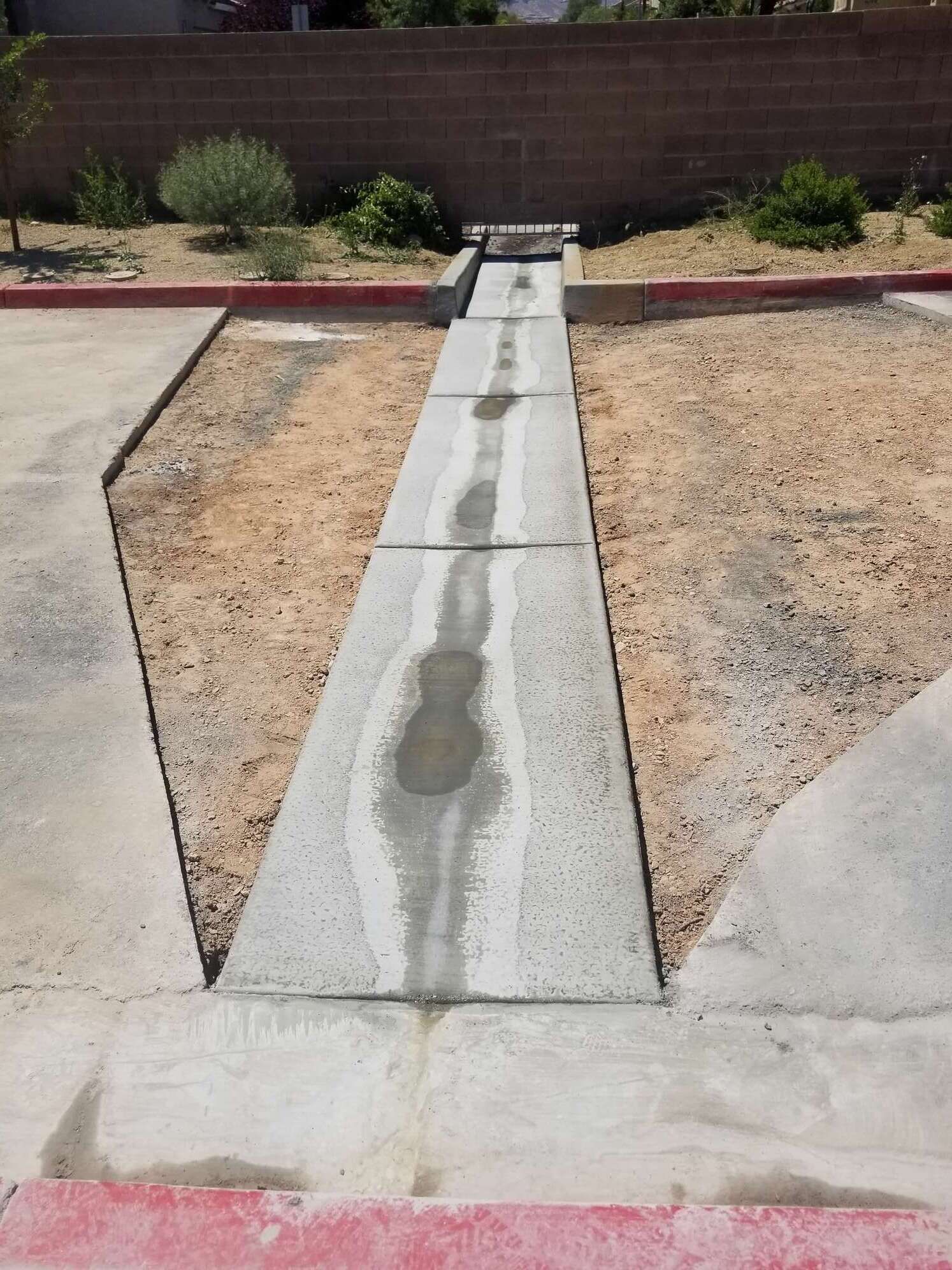 Concrete drainage channel with water flowing through, bordered by gravel and concrete.