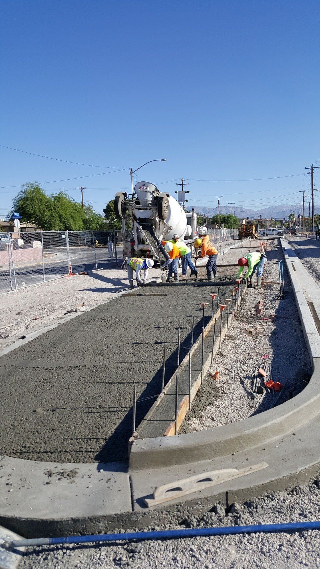 Construction workers pouring concrete from a truck into a form for a sidewalk on a sunny day.