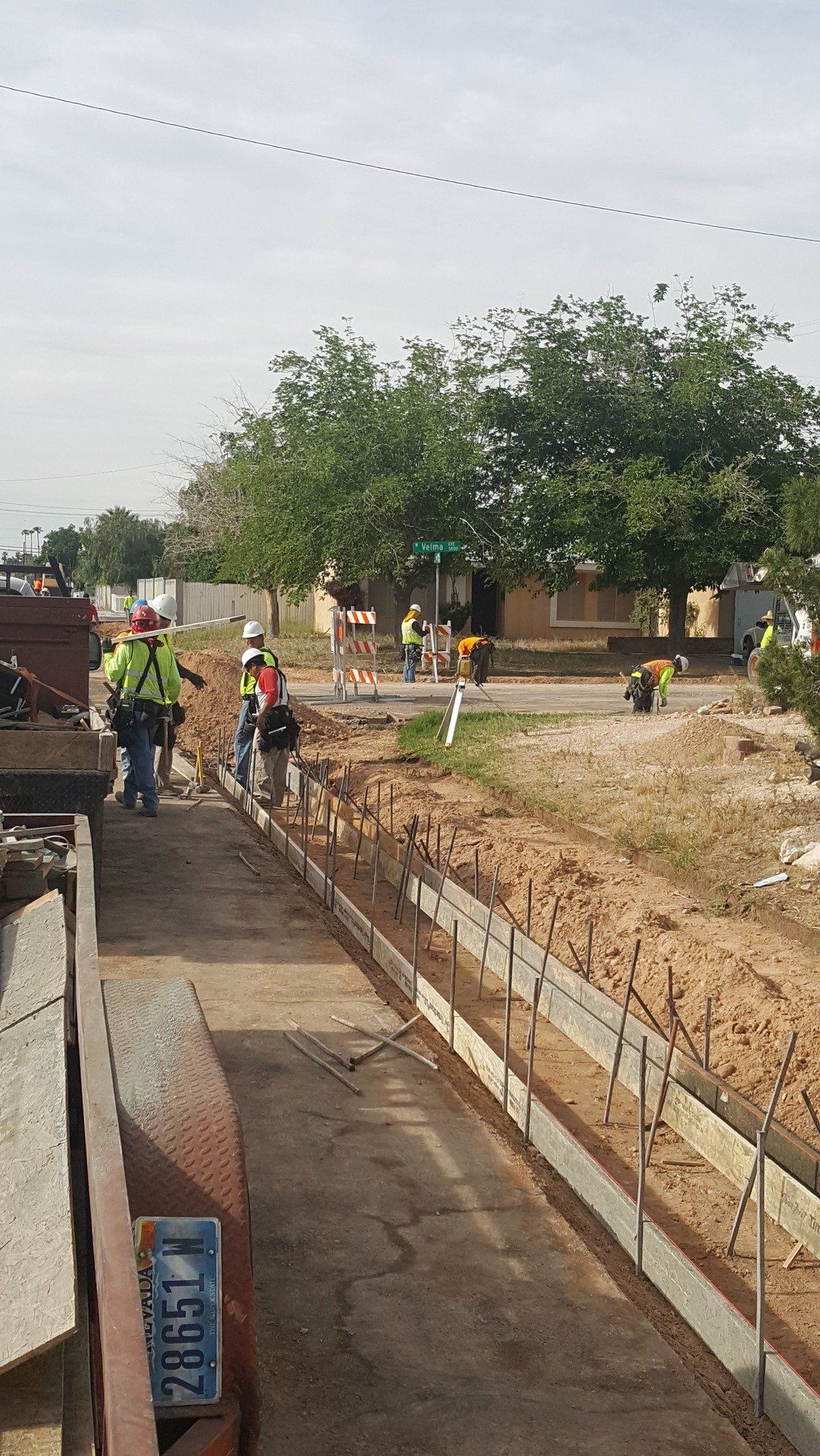 Construction workers at a roadside concrete project. A dirt median has wood forms set up. Workers are present.