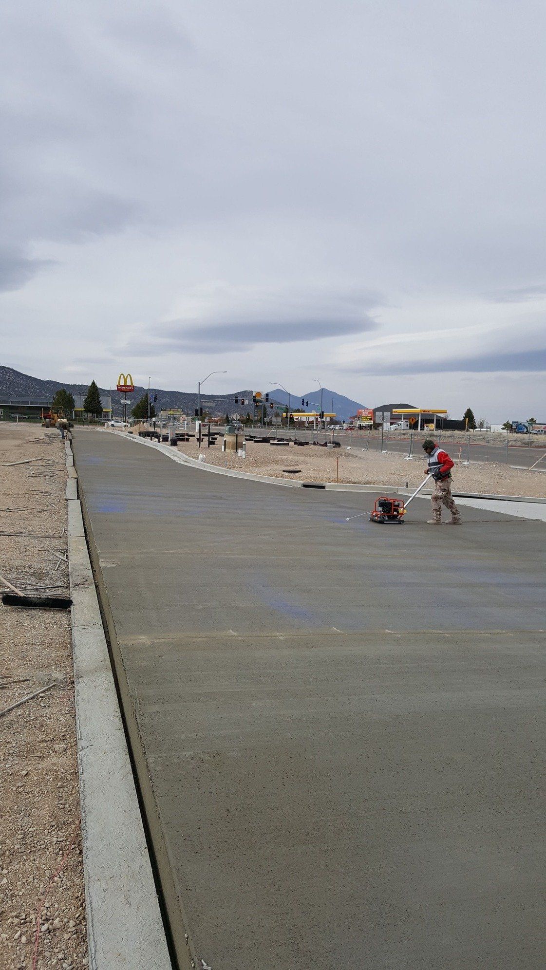 Construction workers working on a freshly poured concrete road. Grey overcast sky with buildings in the background.
