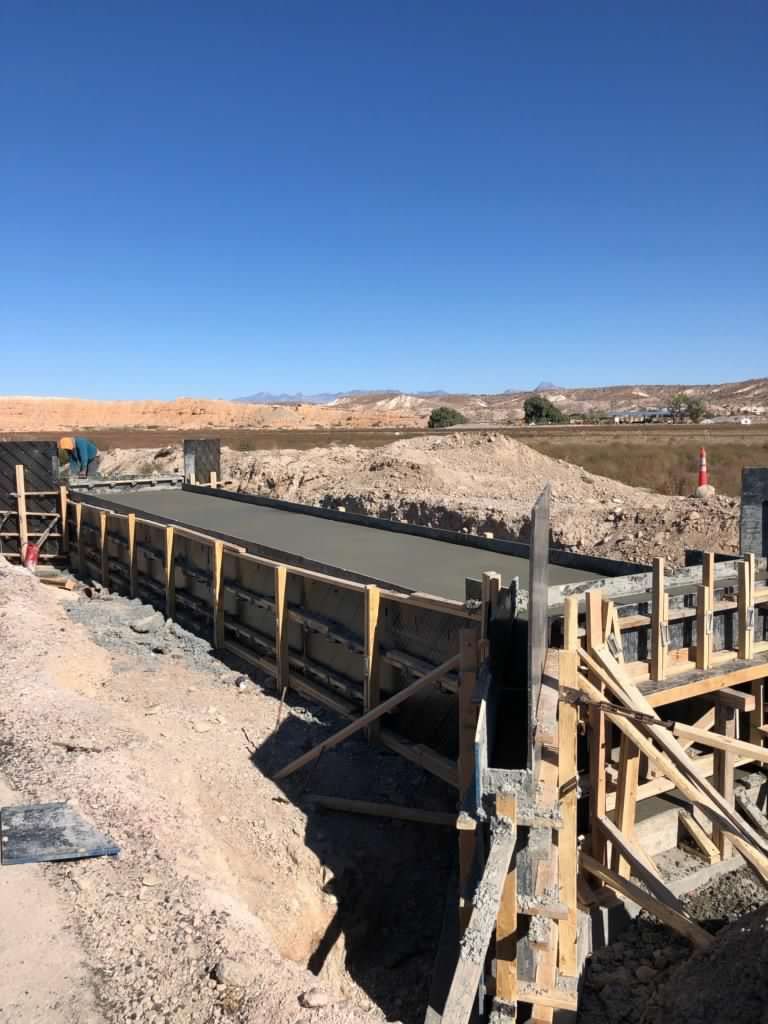 Construction site with a concrete form filled with wet concrete, under a blue sky.