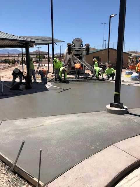 Construction workers pouring concrete at a park.  A cement mixer is pouring, while workers smooth the surface on a sunny day.