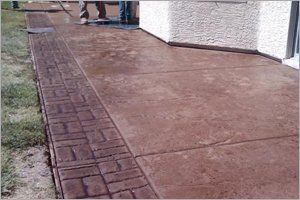 Brown stamped concrete sidewalk with a brick border, being cleaned with a hose.