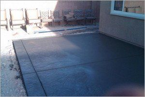 Newly poured concrete patio with chairs in the background next to a building.