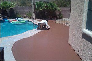 Man smoothing brown concrete patio next to a pool.