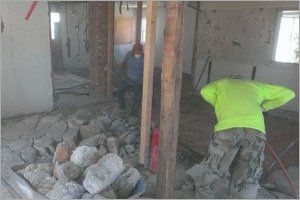 Construction workers inside a building undergoing demolition, debris on the floor, supporting wooden beams.