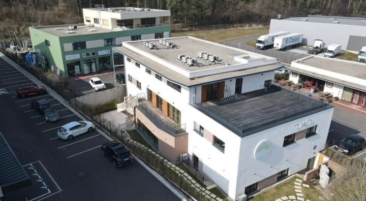 Vue extérieure de trois bâtiments, avec un parking devant. Journée ensoleillée.